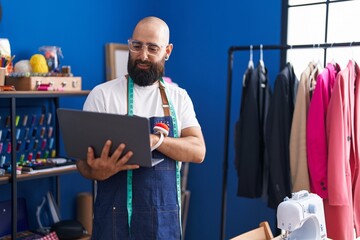 Poster - Young bald man tailor smiling confident using laptop at clothing factory