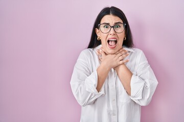 Canvas Print - Young brunette woman standing over pink background shouting and suffocate because painful strangle. health problem. asphyxiate and suicide concept.