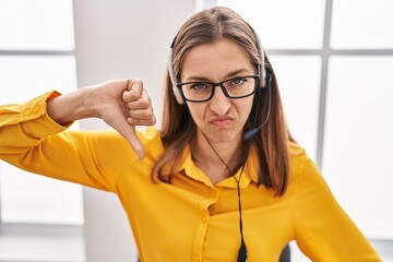 Canvas Print - Young woman wearing call center agent headset with angry face, negative sign showing dislike with thumbs down, rejection concept