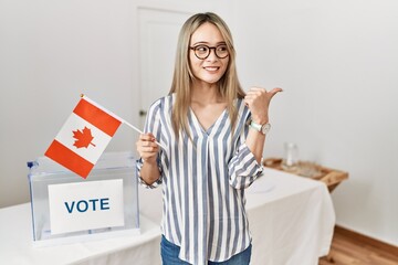 Poster - Asian young woman at political campaign election holding canada flag pointing thumb up to the side smiling happy with open mouth