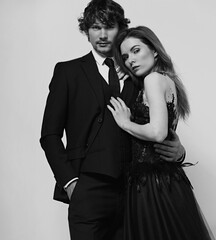 Sexy bright foxy hairstyle female woman in fashion black long skirt wedding dress hugging her handsome man in black luxury suit clothing isolated on light studio background. Closeup
