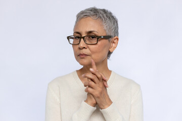 Portrait of doubtful senior woman wearing eyeglasses. Mature Caucasian woman wearing eyeglasses and white jumper looking at camera with uncertainty over white background. Doubt concept