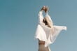 © RooM The Agency - Rear view of a woman dancing outdoors against a blue sky