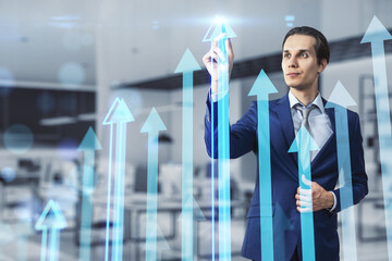 Poster - Attractive young businessman using creative growing arrows chart on blurry office interior background. Return on investment, finance and market growth concept. Double exposure.