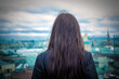 A brunette girl looks at the city from the roof of the house, rear view