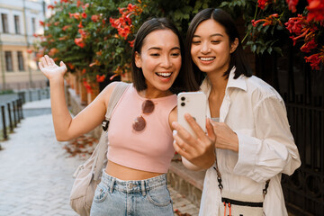 Wall Mural - Two asian women taking selfie photo on cellphone on city street