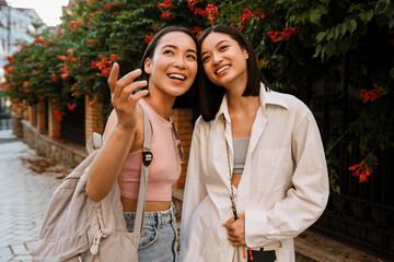 Wall Mural - Two asian women talking and smiling while standing on street