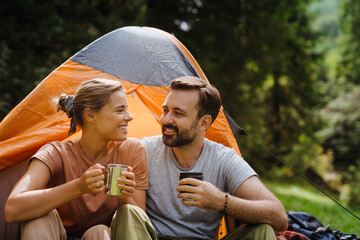 Wall Mural - White young couple drinking tea resting by tent in green forest