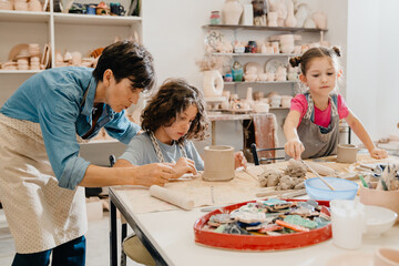 Wall Mural - Mature female teacher assisting group of kids at ceramics workshop