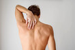 © vikarayu - Young fit man standing with naked muscular back and touching his shoulder with the hand. Back pain and spine issues concept.
