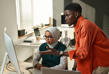 Young confident businessman consulting with Muslim female colleague during presentation of online information or project points