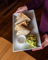 Wall Mural - Woman holding a plate of Garden quesadillas with a side of bacon guacamole and white sauce