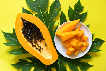 Wall Mural - papaya fruits on yellow backgroud, fresh ripe papaya slice tropical fruit with papaya seed and leaf leaves from papaya tree - top view