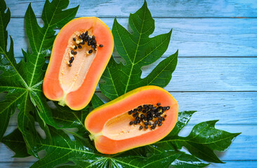 Wall Mural - papaya fruits on blue backgroud, fresh ripe papaya slice cut in half tropical fruit with papaya seed and leaf leaves from papaya tree - top view