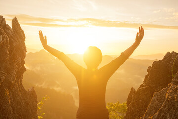 The boy raised his arms on the mountain and the sun was rising.