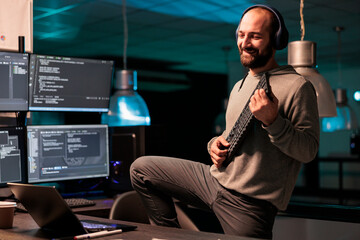 App developer singing and playing guitar with keyboard, using IT equipment and fooling around. Silly funky programmer celebrating success, wokring on server code after hours in office.