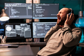 Funny programmer screaming and listening to music on headset, working on app developing software late at night. Web developer singing song in office, coding online cloud database.