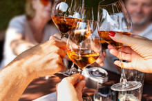 Family Celebrating At Dinner. Detail Of Hands While Toasting With Glasses Of Orange Wine In A Sunny Day.
