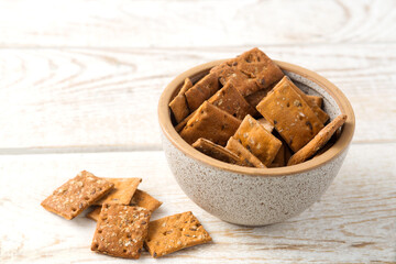 Bowl of dry crackers with tomato and basil taste on light wood background. close-up