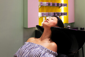 Wall Mural - young woman waiting in the hairdressing area of a beauty salon to have her hair washed, concept of wellness and hair care