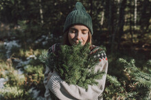 Woman With Eyes Closed Smelling Twigs Of Evergreen Tree In Forest