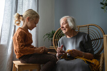 Smiling Senior Woman Looking At Granddaughter Holding Knitting Needle In Living Room
