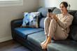 © Westend61 - Woman using smart phone wearing headphones listening to music on sofa at home