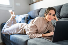 Young Woman Watching Movie On Laptop Lying On Couch At Home