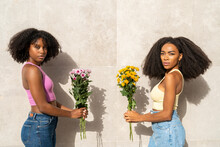 Woman With Friend Holding Flowers In Front Of White Wall