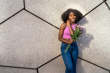 Happy Woman Holding Purple Flowers In Front Of Wall