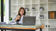 © bongkarn - Charming caucasian businesswoman holding a coffee cup, sitting at her office desk