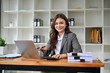 © bongkarn - Beautiful Caucasian businesswoman sitting at her desk, smiling and looking at camera.