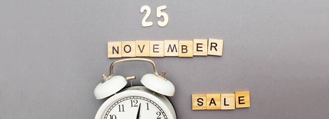 inscription November 25 sale made by wooden cubes and alarm clock on a grey background. banner