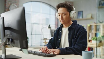 Fototapete - Portrait of Asian Male Employee Working on Computer in a Modern Office During the Day. Customer Support Agent Answering Requests While Using Headphones. Handheld Shot.
