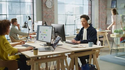 Fototapete - Multiethnic Creative Colleagues Working Using Computers in an Open Office During Day Time. Asian Man Listening to a Meeting on Headphones. Female Director working on a Schedule. Handheld Shot.