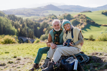 Wall Mural - Senior couple having break,sitting with binoculars during hiking in autumn nature.