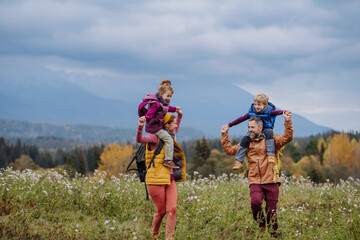 Wall Mural - Happy parents with their little kids on piggyback at autumn walk, in the middle of colourfull nature. Concept of healthy lifestyle.