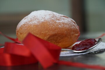 Sticker - Closeup low-angle shot of doughnut with fruity jam and red ribbon on a white cloth on a wooden desk