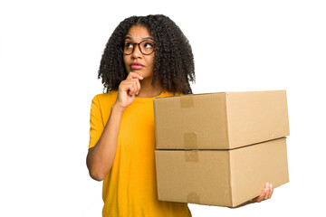 Wall Mural - Young african american woman moving to other house while picking up a box full of things isolated looking sideways with doubtful and skeptical expression.