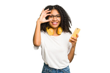 Young african american woman listening to music with yellow headphones isolated excited keeping ok gesture on eye.