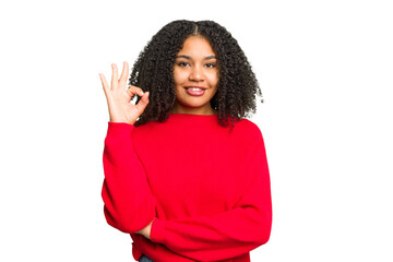 Wall Mural - Young african american woman isolated winks an eye and holds an okay gesture with hand.