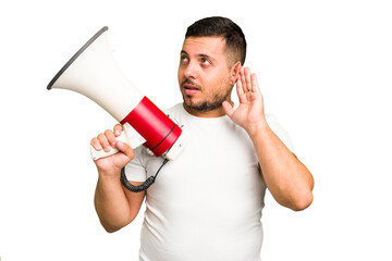 Canvas Print - Young caucasian man holding a megaphone isolated trying to listening a gossip.