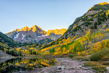 Maroon Bells Lake At Sunrise Sunlight In Aspen, Colorado With Rocky Mountain Peak And Snow In October Autumn And Golden Fall Leaf Color Trees Reflection On Water