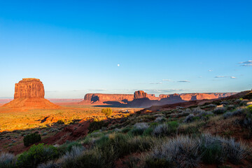 Monument Valley Merrick Butte and horizon at sunset colorful light in Arizona with orange rocks formations and cars driving on scenic loop road with blue sky