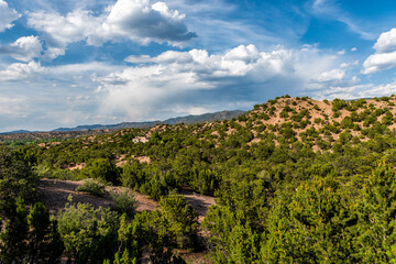 Sunset evening in Santa Fe, New Mexico Tesuque community neighborhood in Rocky Mountain foothills with houses and green plants pinyon trees shrubs and blue sky clouds