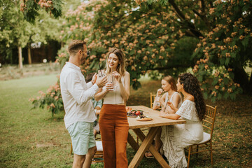 Group of happy young people cheering with fresh lemonade and eating fruits in the garden