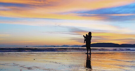 Wall Mural - Silhouette of happy family mother playing carrying cute baby daughter at the beach during amazing sunset enjoying their vacation together at ao nang beach, krabi Thailand