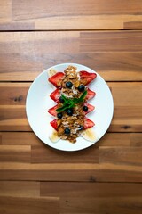 Sticker - Vertical closeup of delicious fruit salad with oat flakes and mint leaves on a white plate