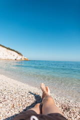 Wall Mural - Successful man lies and rest on a white stone beach by a blue sea with clear water and rock on the island of Elba, Italy