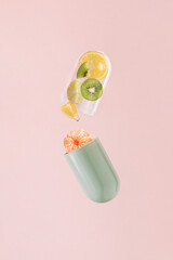 green transparent pill with lemon, tangerine, kiwi and lime on isolated pastel coral pink background